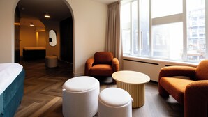 Ein modernes Hotelzimmer mit einem Bett, zwei Poufs, einem runden Couchtisch und einer Couch.