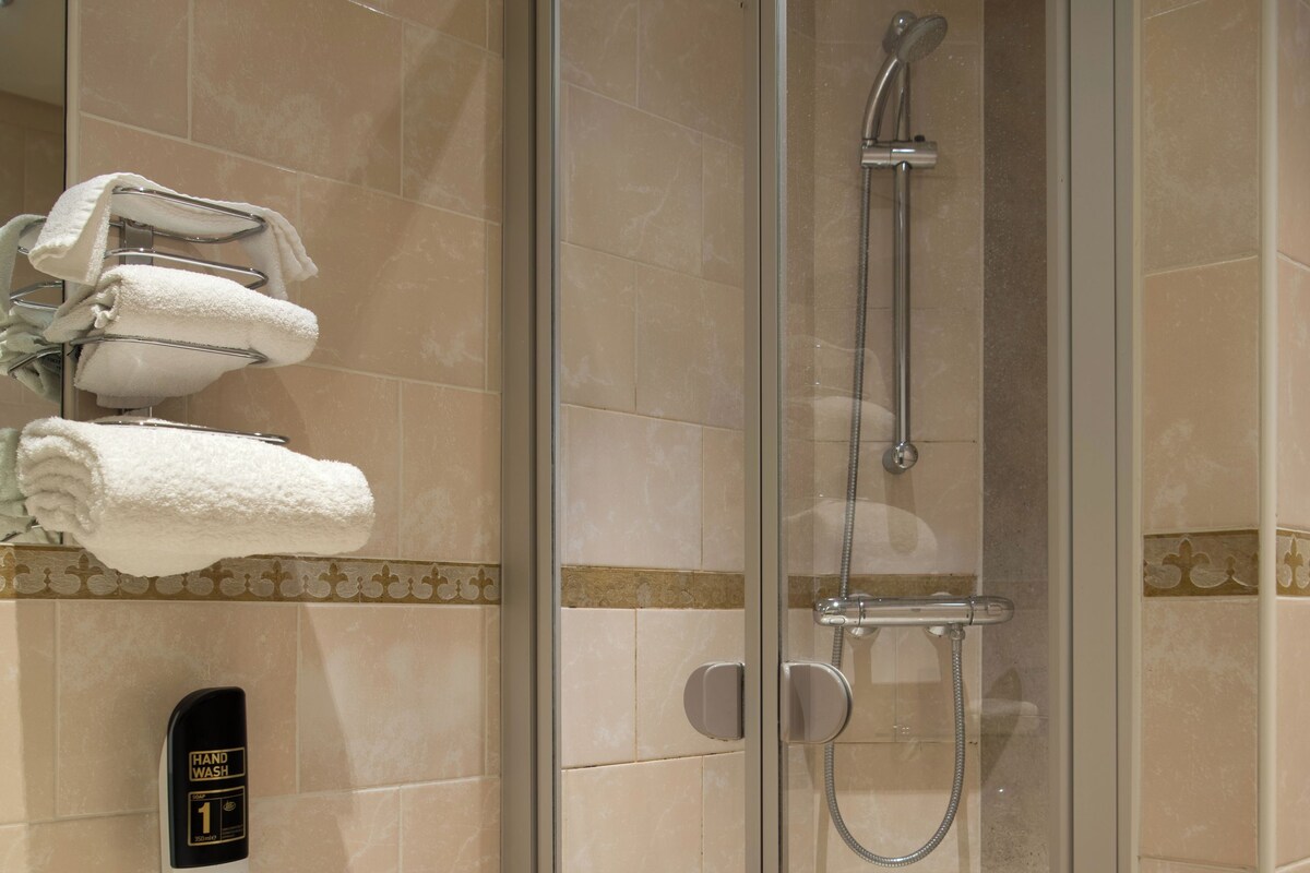 A modern bathroom with a glass-enclosed shower, a white sink, and a hand wash station.