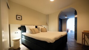Ein Schlafzimmer mit Bett, Nachttisch, Toilette und einem zur anderen Kammer führenden Gang.