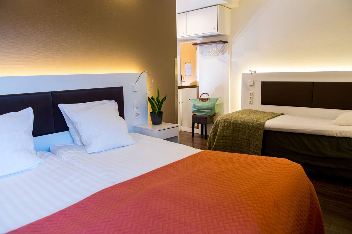 A hotel room with two beds, a desk with a lamp, a potted plant, and a small seating area.