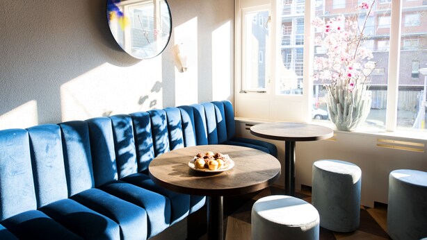 Ein modernes Interieur mit einer blauen Sitzbank, einem runden Tisch mit Speisen und einem Blumenstrauß an einem Fenster.