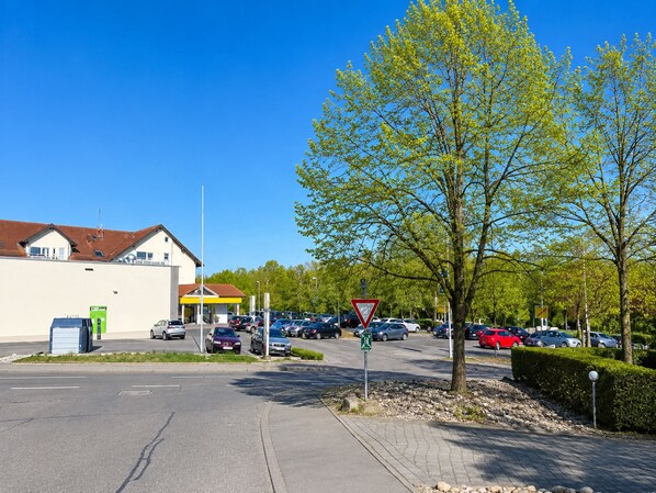 A parking lot with cars, a pedestrian crossing, and a building with a red roof.