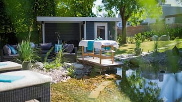 A serene outdoor setting with a small wooden deck, a massage table, and a pond.