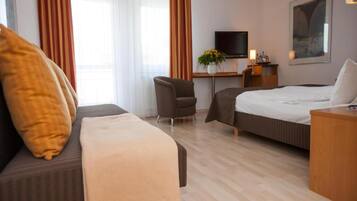 Habitación de hotel con cama, sofá, escritorio con silla, televisión y un cuadro en la pared.
