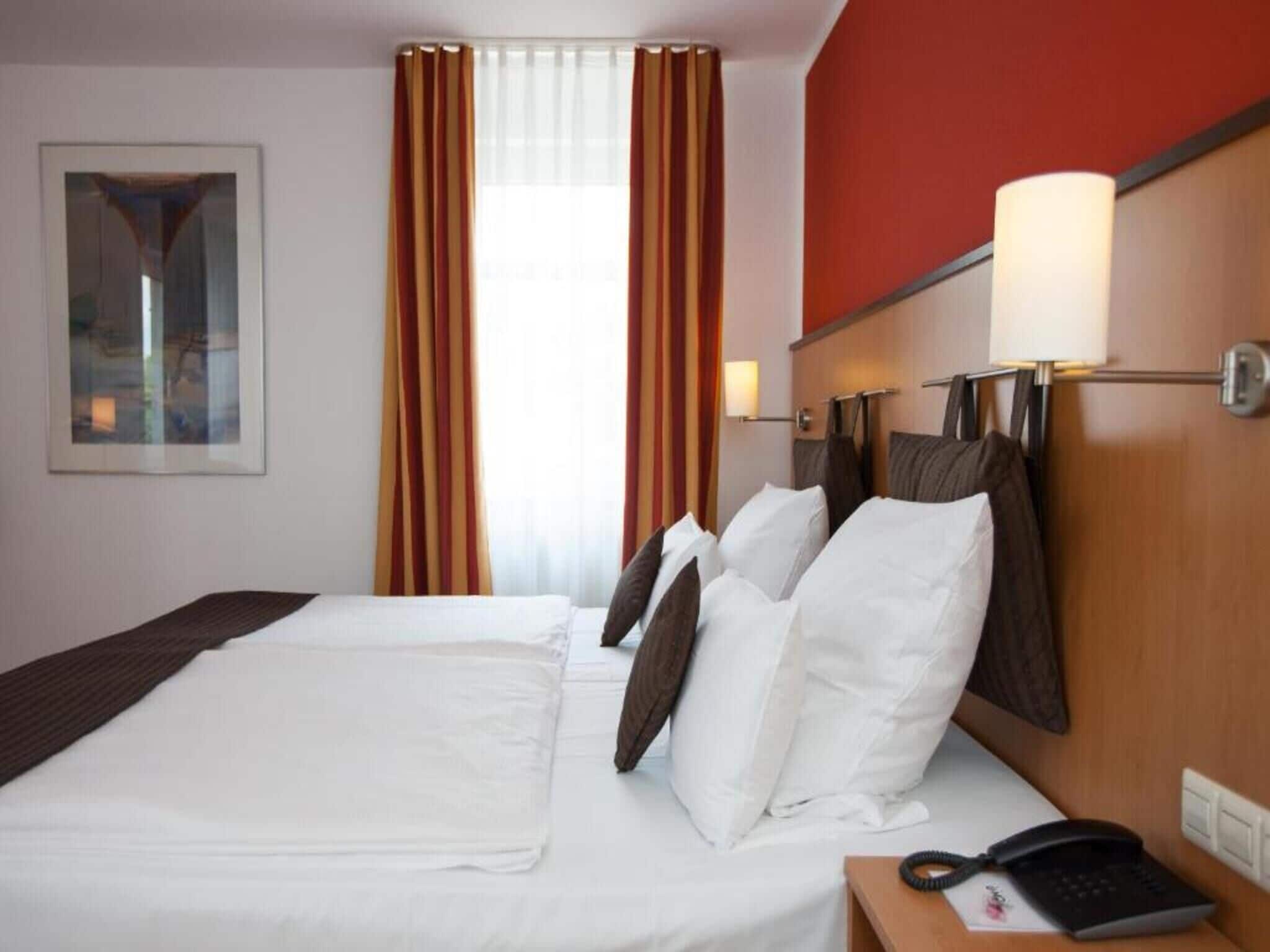 Habitación de hotel con una cama grande, un teléfono en la mesita de noche y una ventana con cortinas.