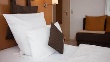 A hotel room with a neatly made bed, a wooden headboard, and a sofa with cushions.