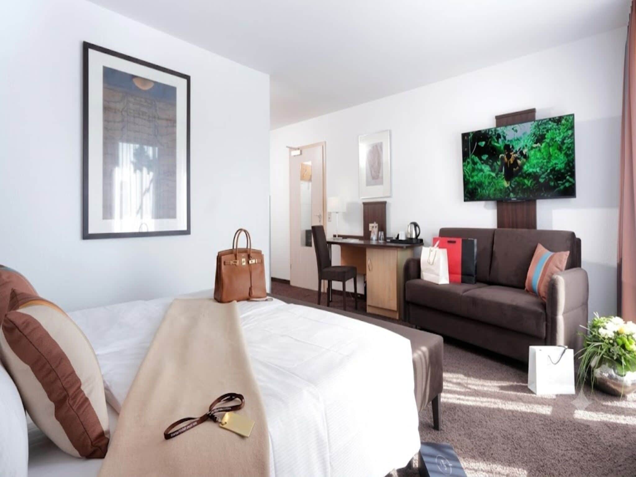 A hotel room with a bed, a desk, a sofa, a television, and a window.