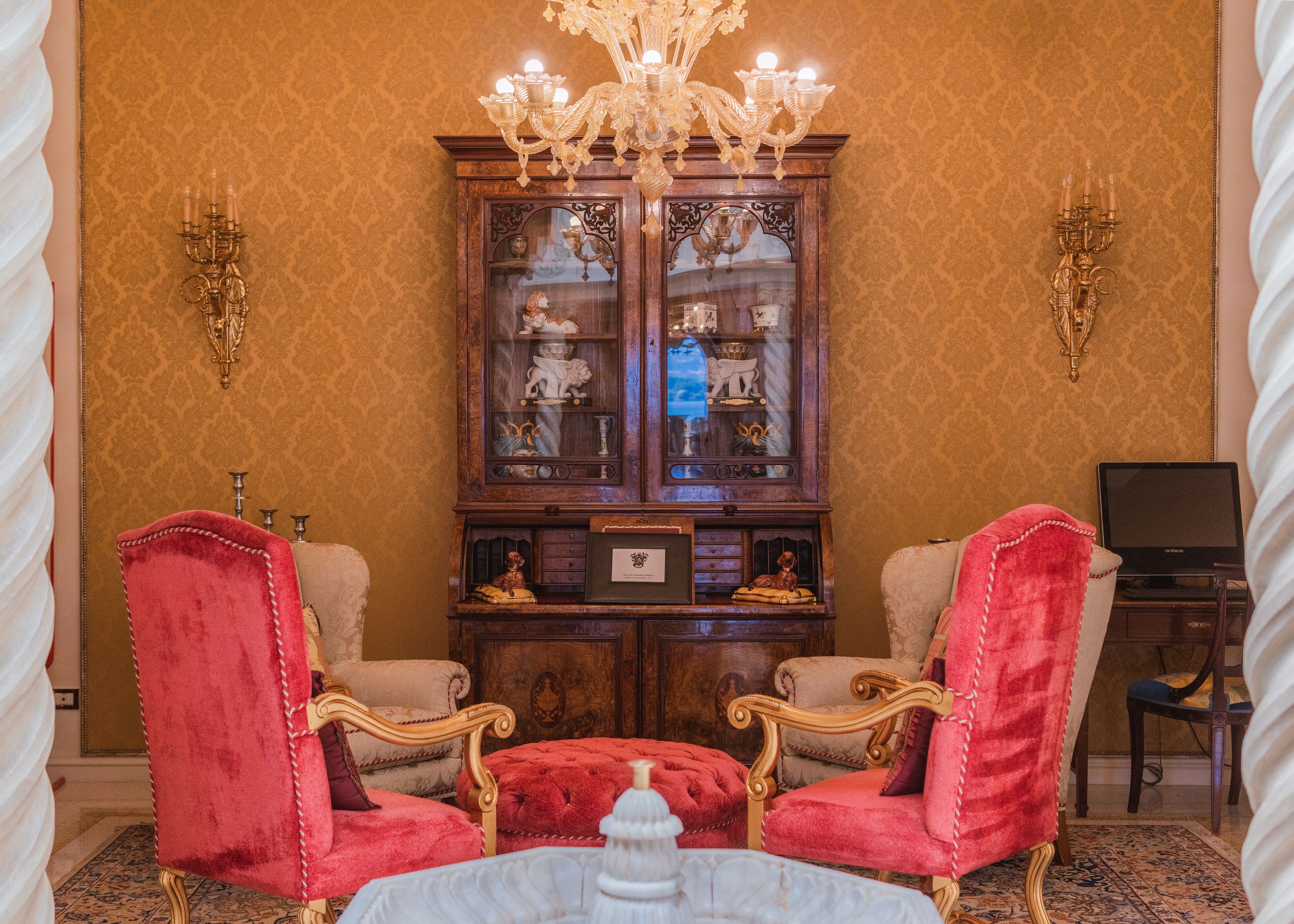 Une pièce avec deux fauteuils à bras en velours rouge, un buffet en bois aux portes vitrées et un lustre.