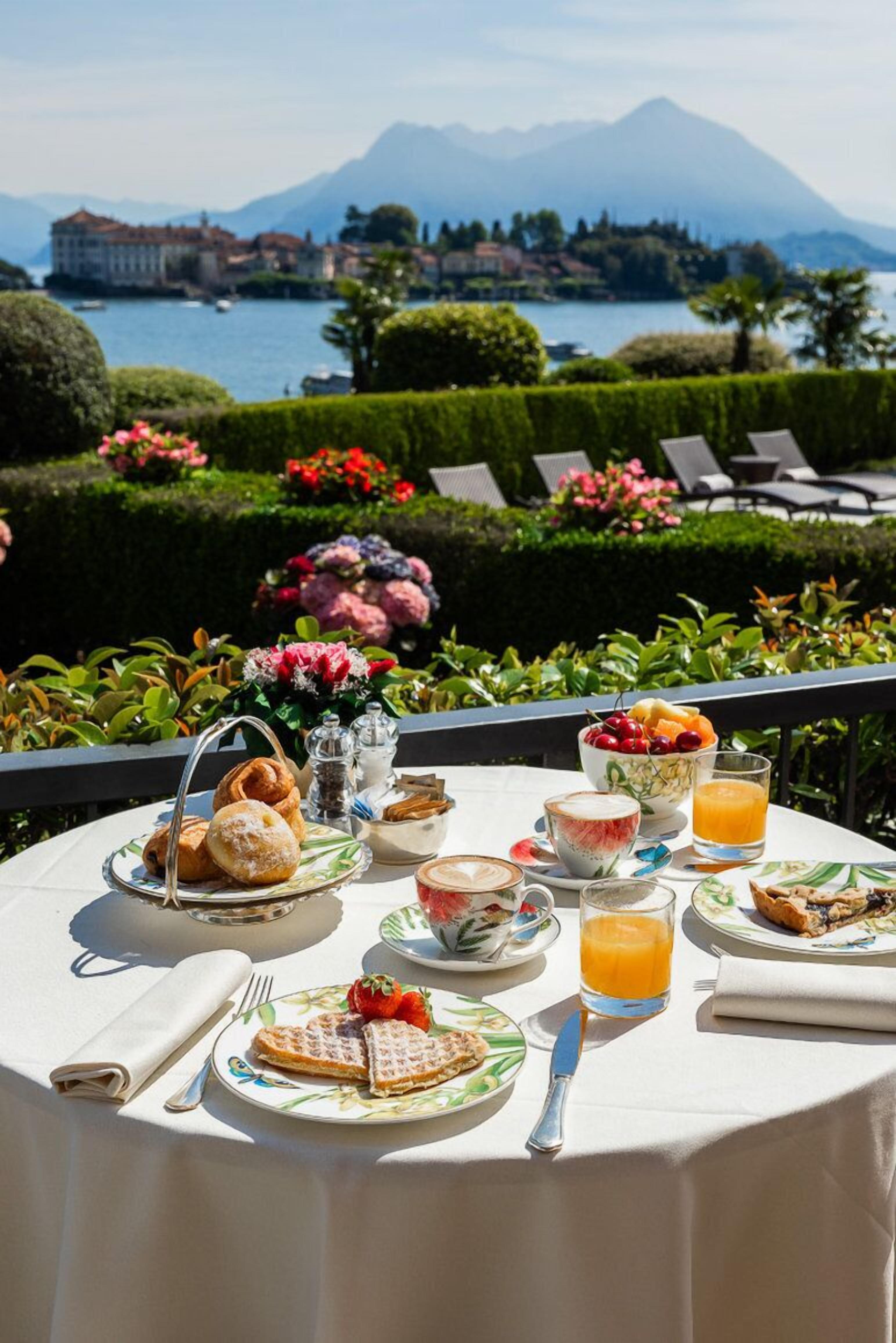 Ein Tisch ist reichhaltig mit Frühstück zubereitet, mit Waffeln, Gebäck und Obst, mit Blick auf einen malerischen See und Berge.