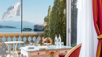 Ein Balkon mit Tisch für zwei Personen, mit Blick auf einen See, eine Flagge und ein Gebäude im Hintergrund.