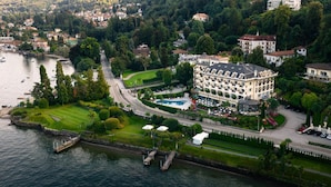 An aerial view of a hotel with a swimming pool, surrounded by greenery and a lake.