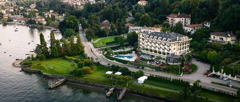 An aerial view of a hotel with a swimming pool, surrounded by greenery and a lake.
