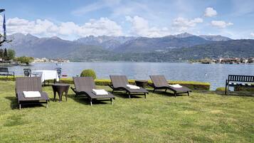 A lakeside lounge area with wicker lounge chairs and a small table, overlooking a lake and mountains.