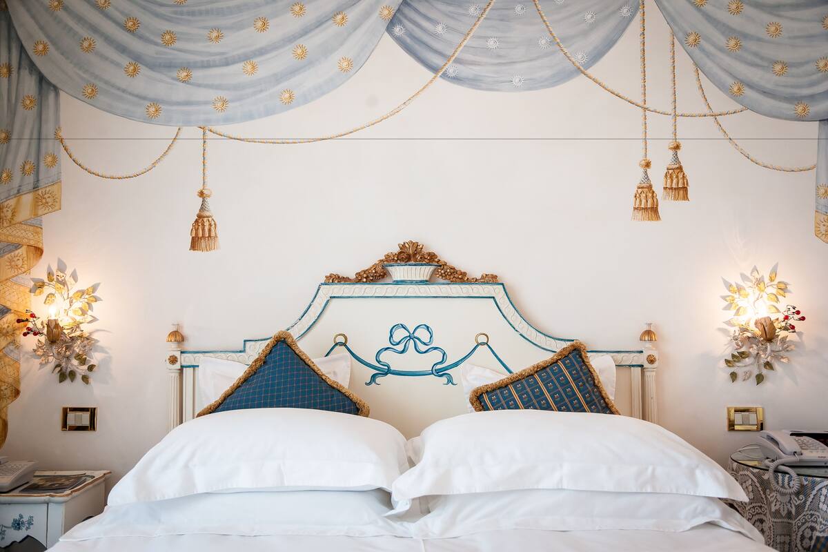 A neatly made bed with white linens and blue pillows, a decorative headboard, and hanging tassels.