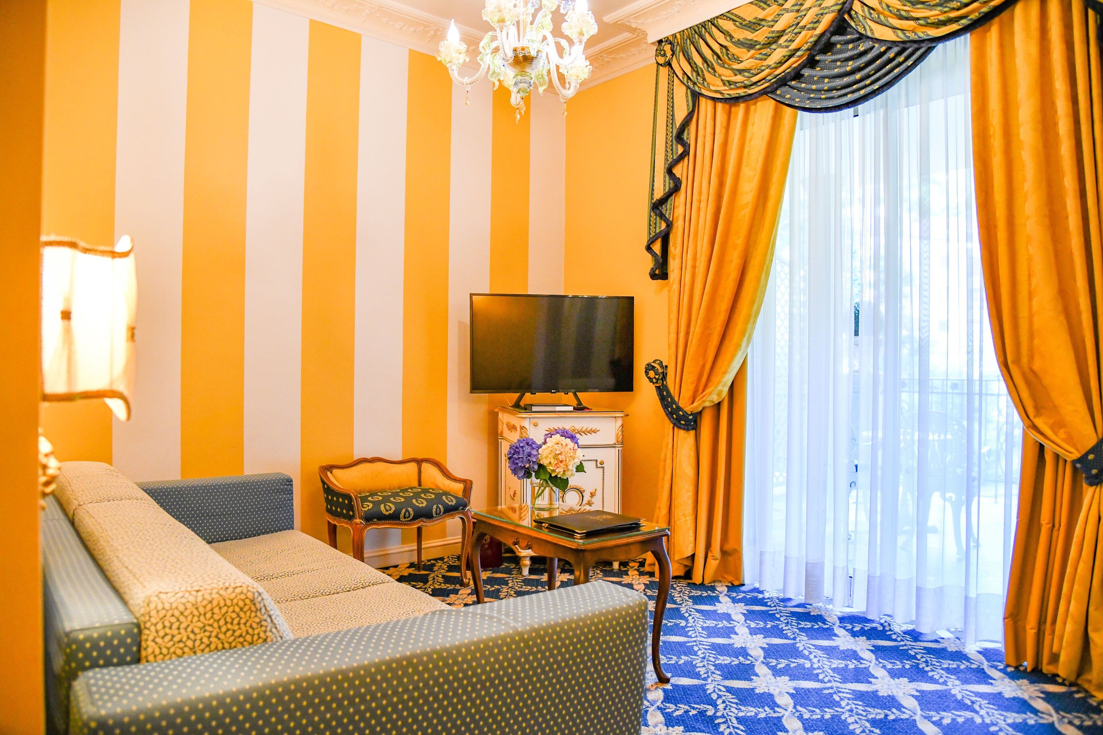 A room with a sofa, a television, and a table with a vase of flowers.