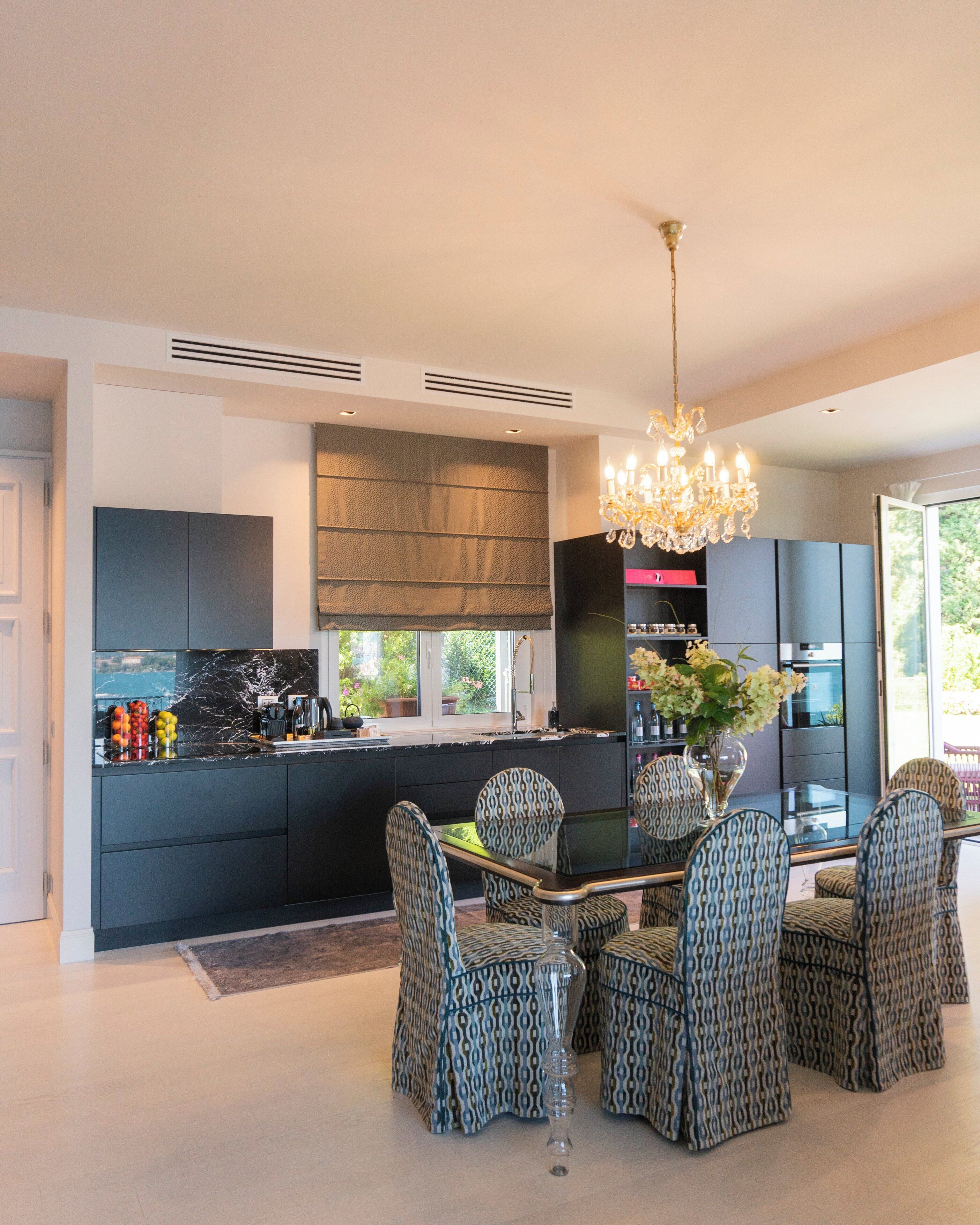 A modern kitchen with dark cabinetry, a central island, patterned chairs, and a chandelier.