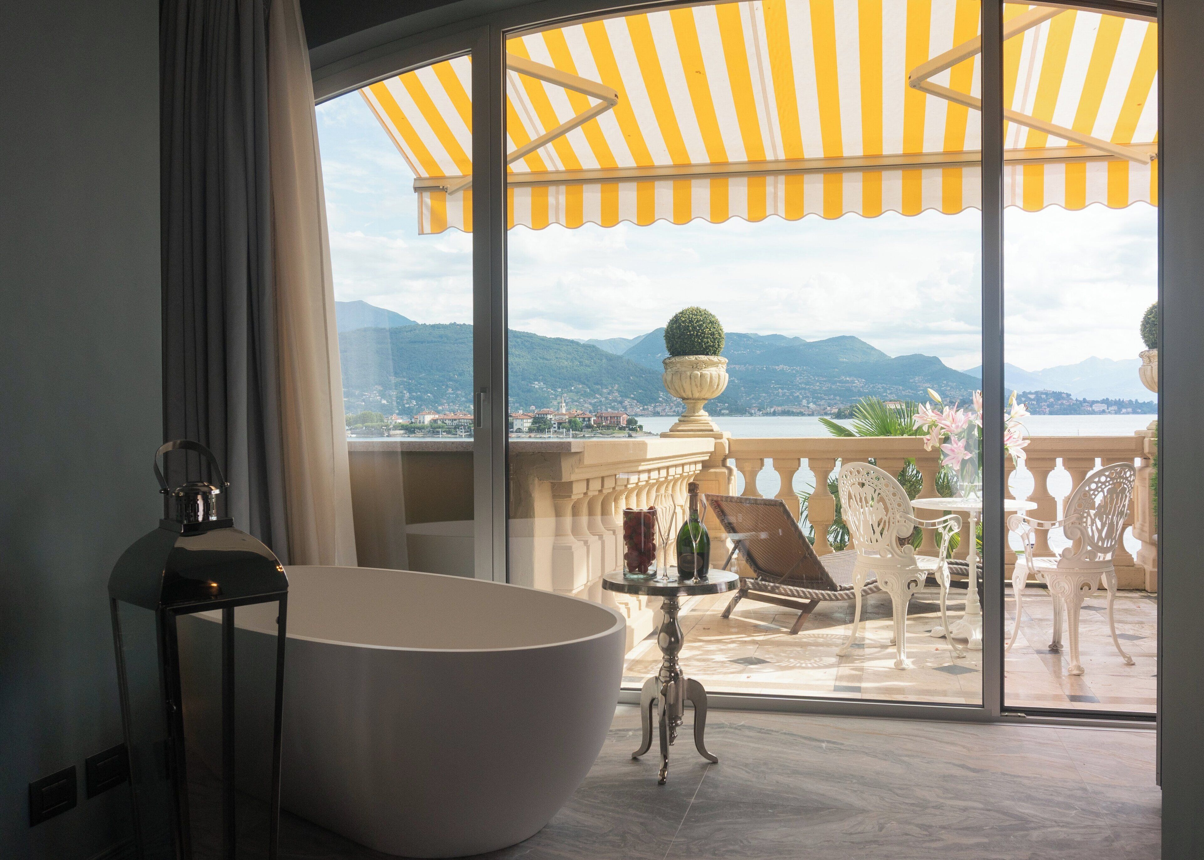 Ein Badezimmer mit einer großen Badewanne, einer Duschkabine und Blick auf einen Balkon mit Gartenmöbeln und Bergblick.