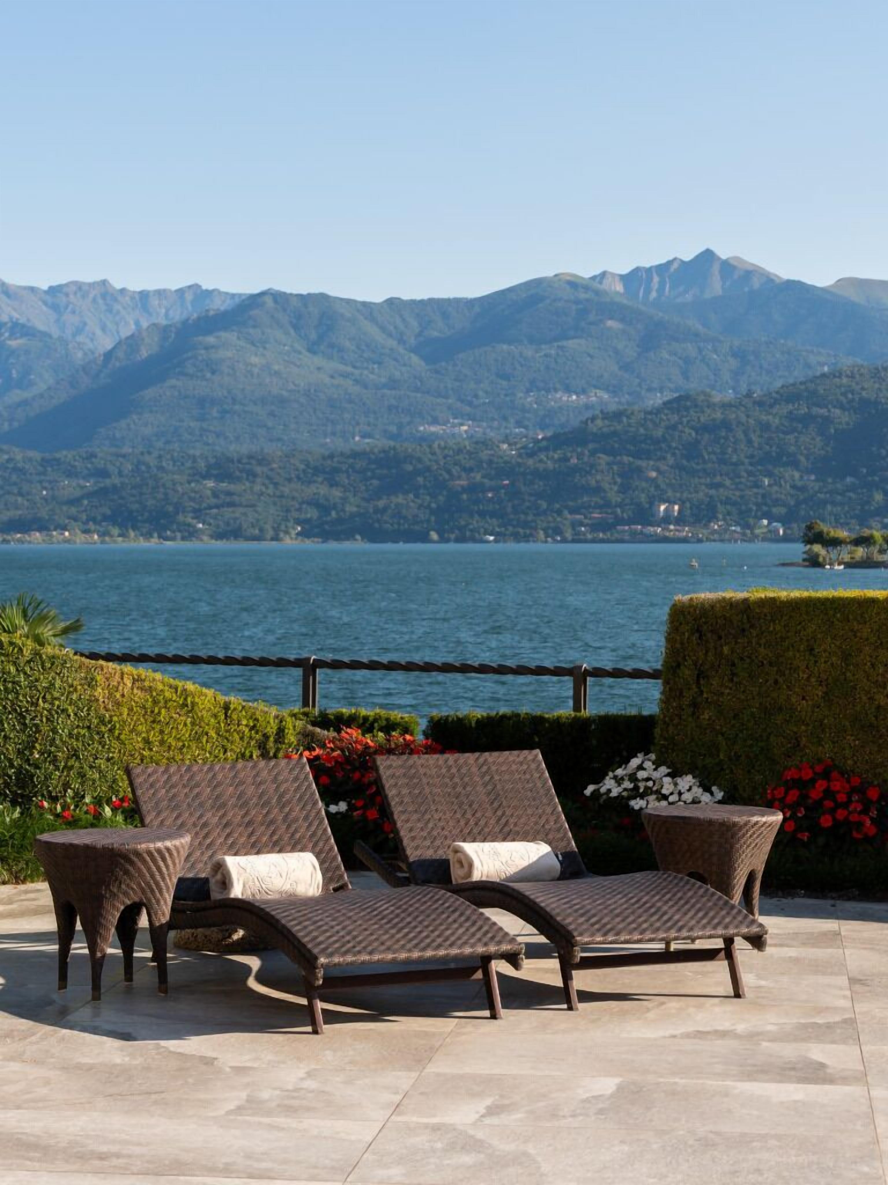 Une terrasse dotée de fauteuils de jardin en osier et offrant une vue sur un lac et des montagnes.