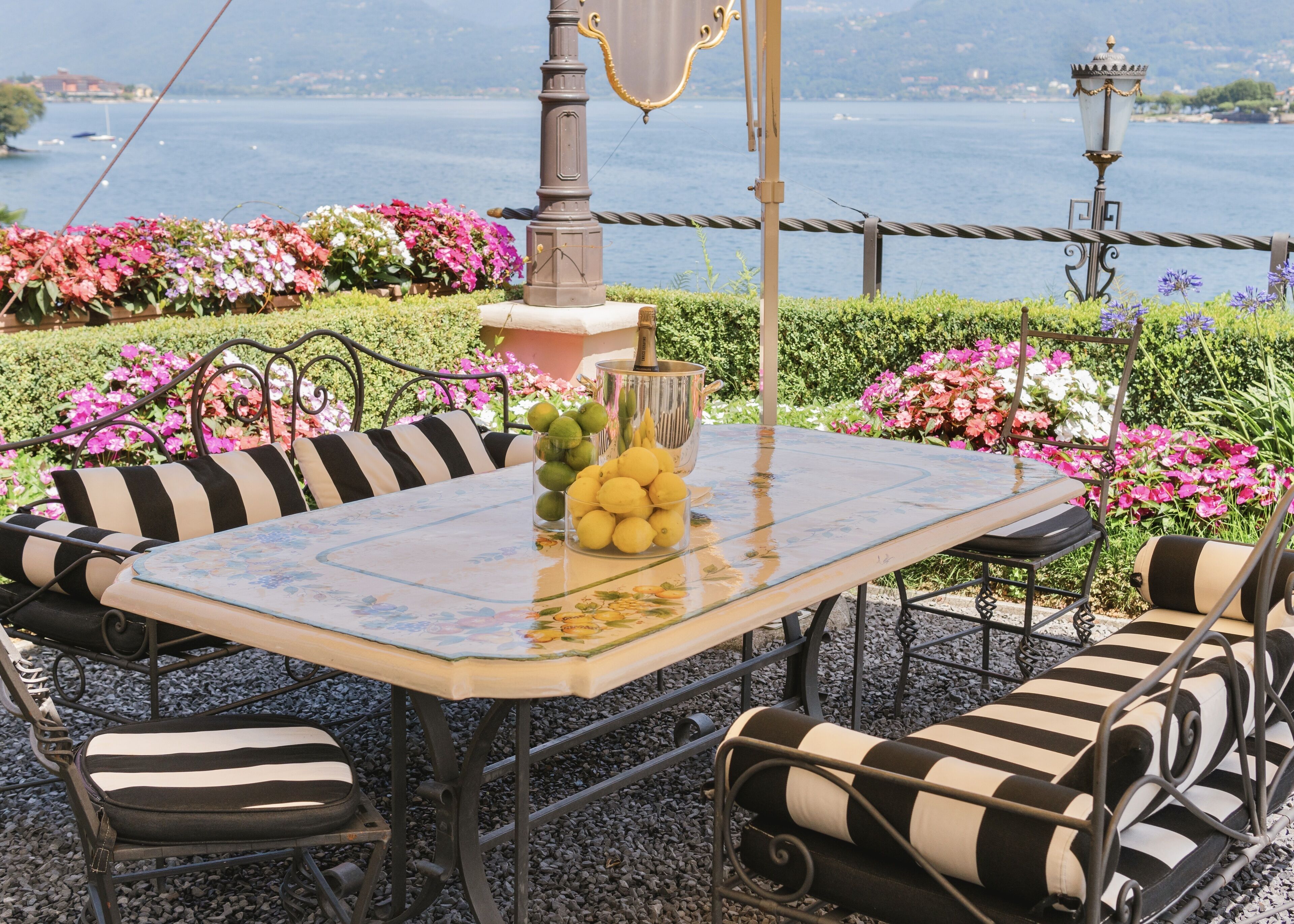 Une table recouverte d’une nappe à motifs floraux, entourée de chaises à coussins rayés, le tout placé devant un paysage pittoresque avec vue sur un lac.