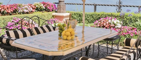 Une table recouverte d’une nappe à motifs floraux, entourée de chaises à coussins rayés, le tout placé devant un paysage pittoresque avec vue sur un lac.