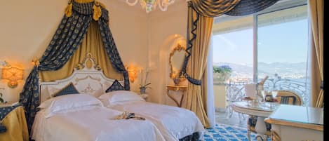 A luxurious bedroom with a large bed, ornate curtains, a chandelier, and a view of the city.