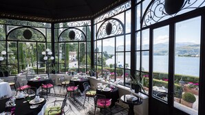 A dining area with tables set for a meal, large windows with decorative ironwork, and a view of a lake and mountains.