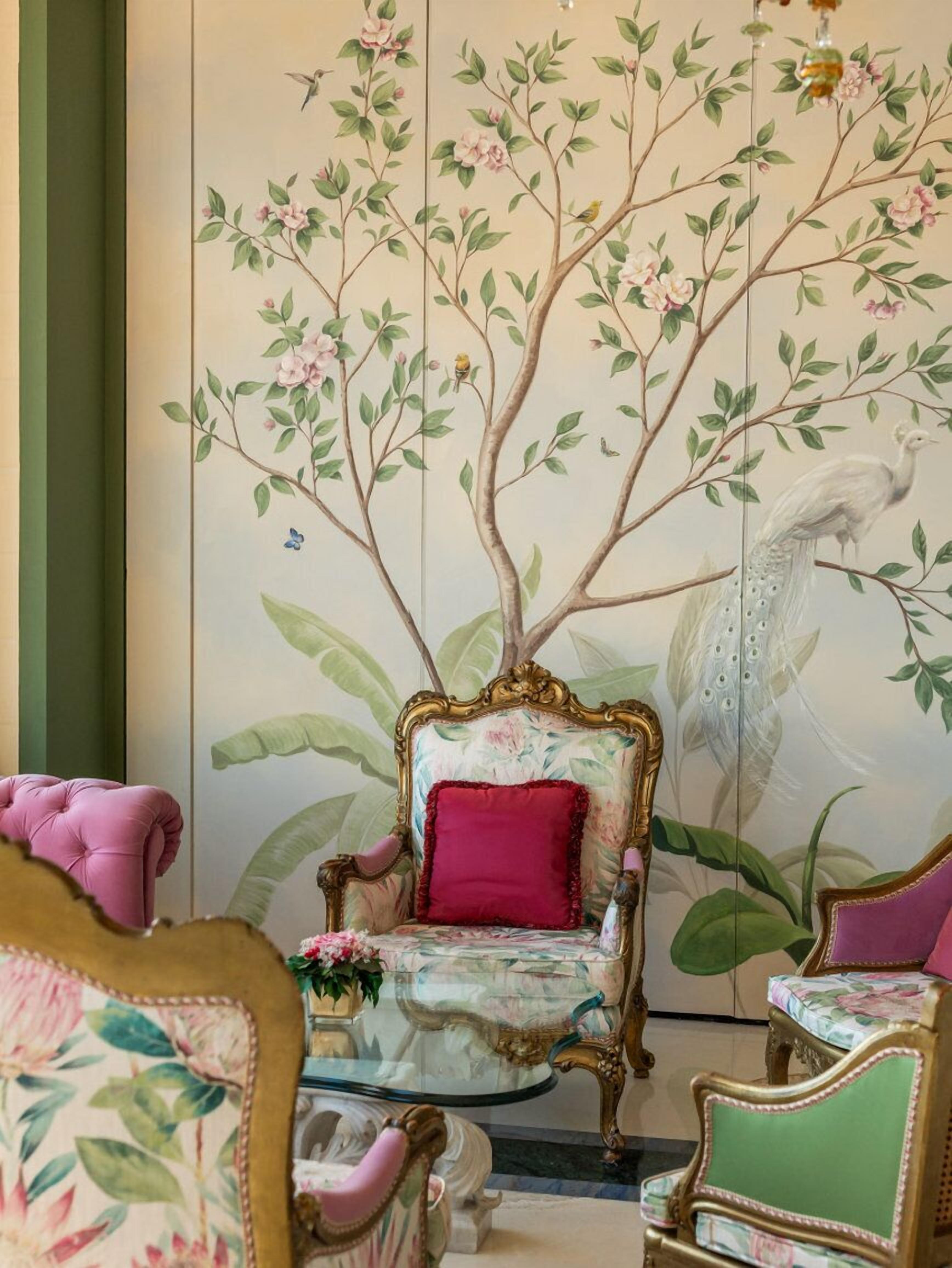 Ein Zimmer mit einer großen Blumenmalerei an der Wand, einem bequemen Sessel mit rotem Kissen und einem kleinen Tisch mit Blumen in einer Vase.