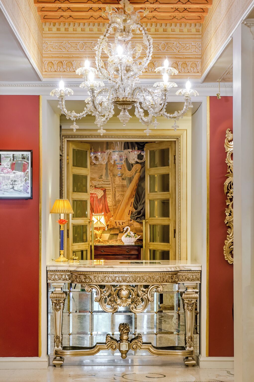 A grand room with a large ornate mirror, a chandelier, and a marble fireplace.