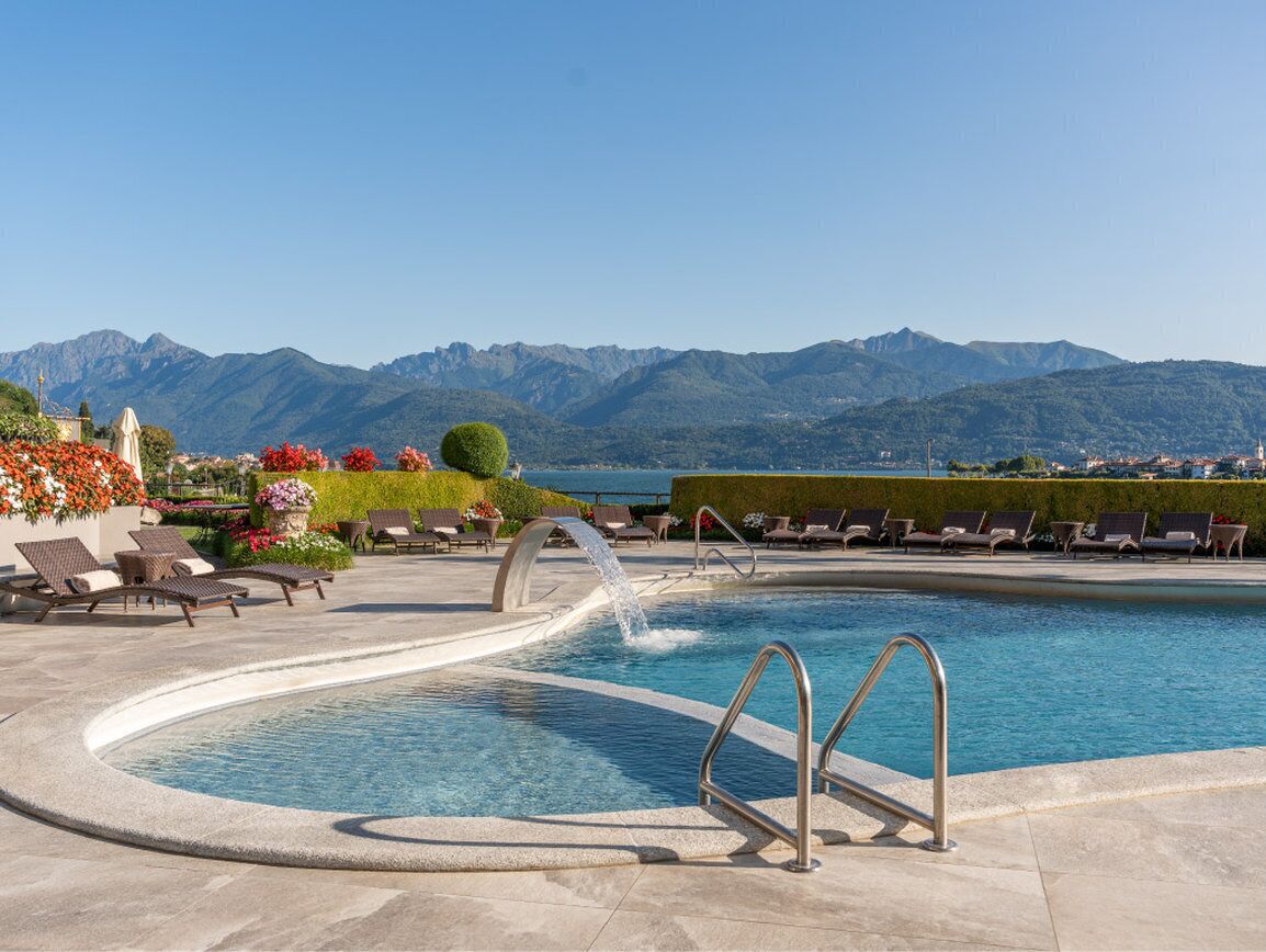 Una piscina con cascata, circondata da sdraio e con vista sulle montagne.