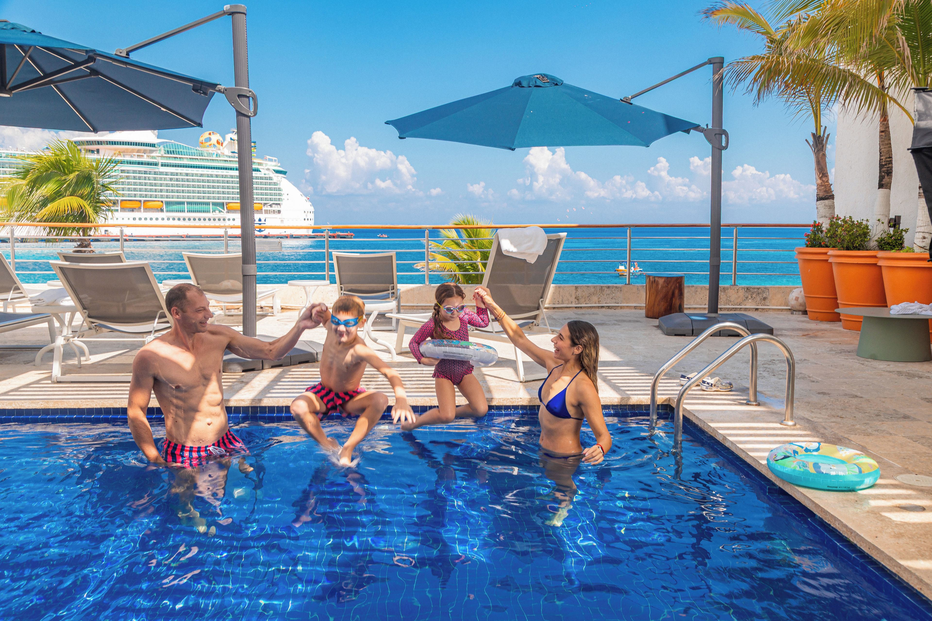 Una piscina con sillones de descanso y sombrillas, un crucero al fondo y una vista despejada del océano.