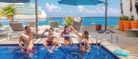 Una piscina con sillones de descanso y sombrillas, un crucero al fondo y una vista despejada del océano.