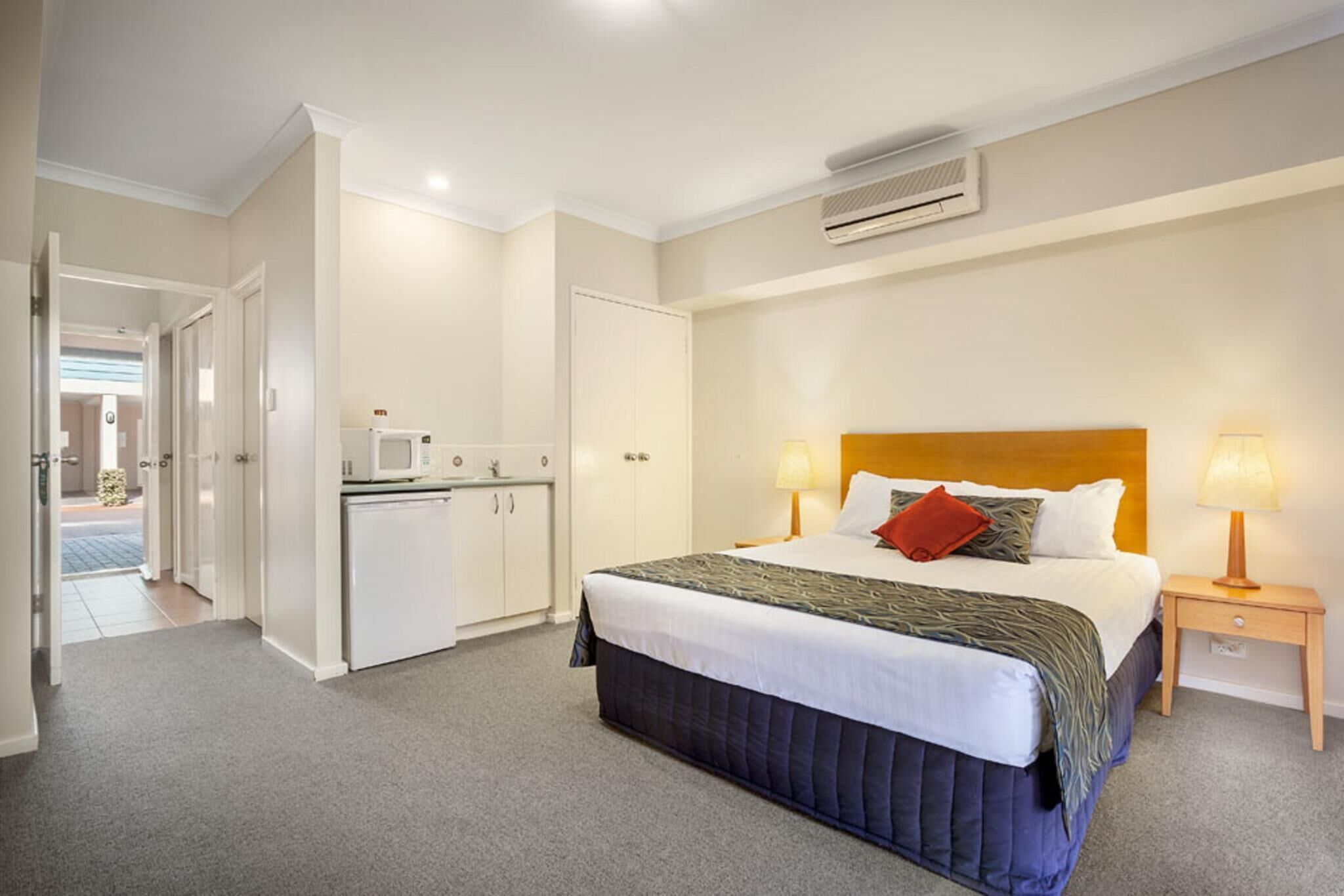 A hotel room with a bed, bedside lamps, a microwave, and a wardrobe.