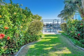 A pathway leading to a pool area surrounded by lush greenery and a clear blue sky. - C Mandurah Resort (Halls Head)