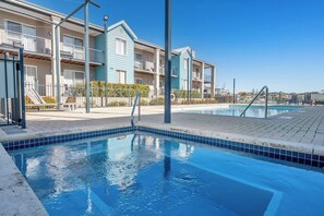 A swimming pool with a tiled edge, a building with balconies, and a clear sky. - C Mandurah Resort (Halls Head)