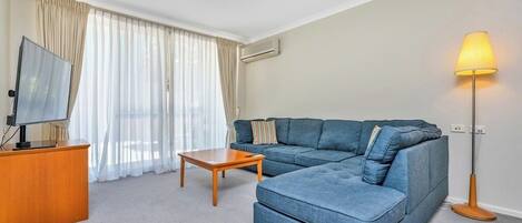 A living room with a sofa, a coffee table, a TV on a stand, and a lamp.