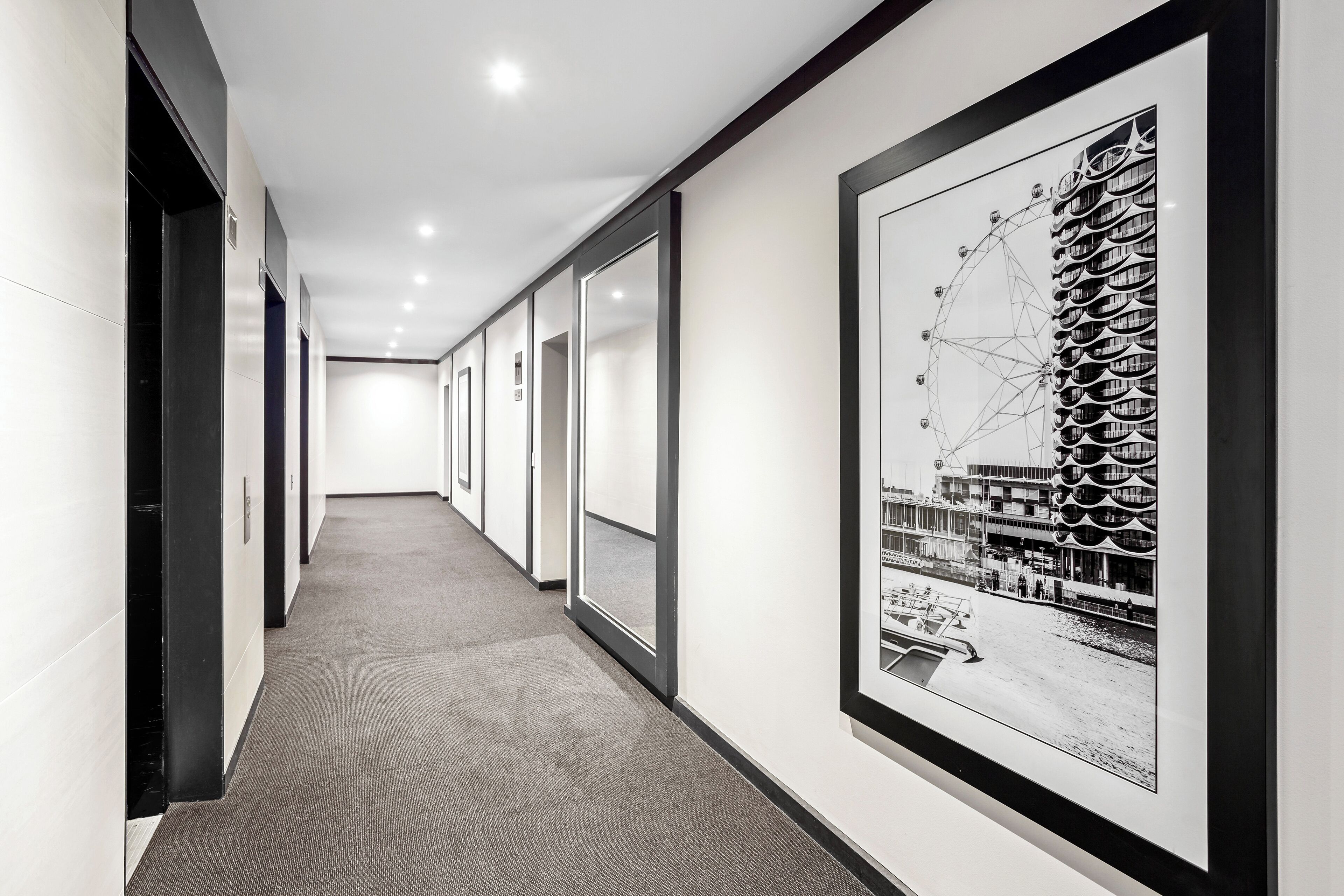 A hallway with a carpeted floor, glass doors, and a framed black and white photograph on the wall.
