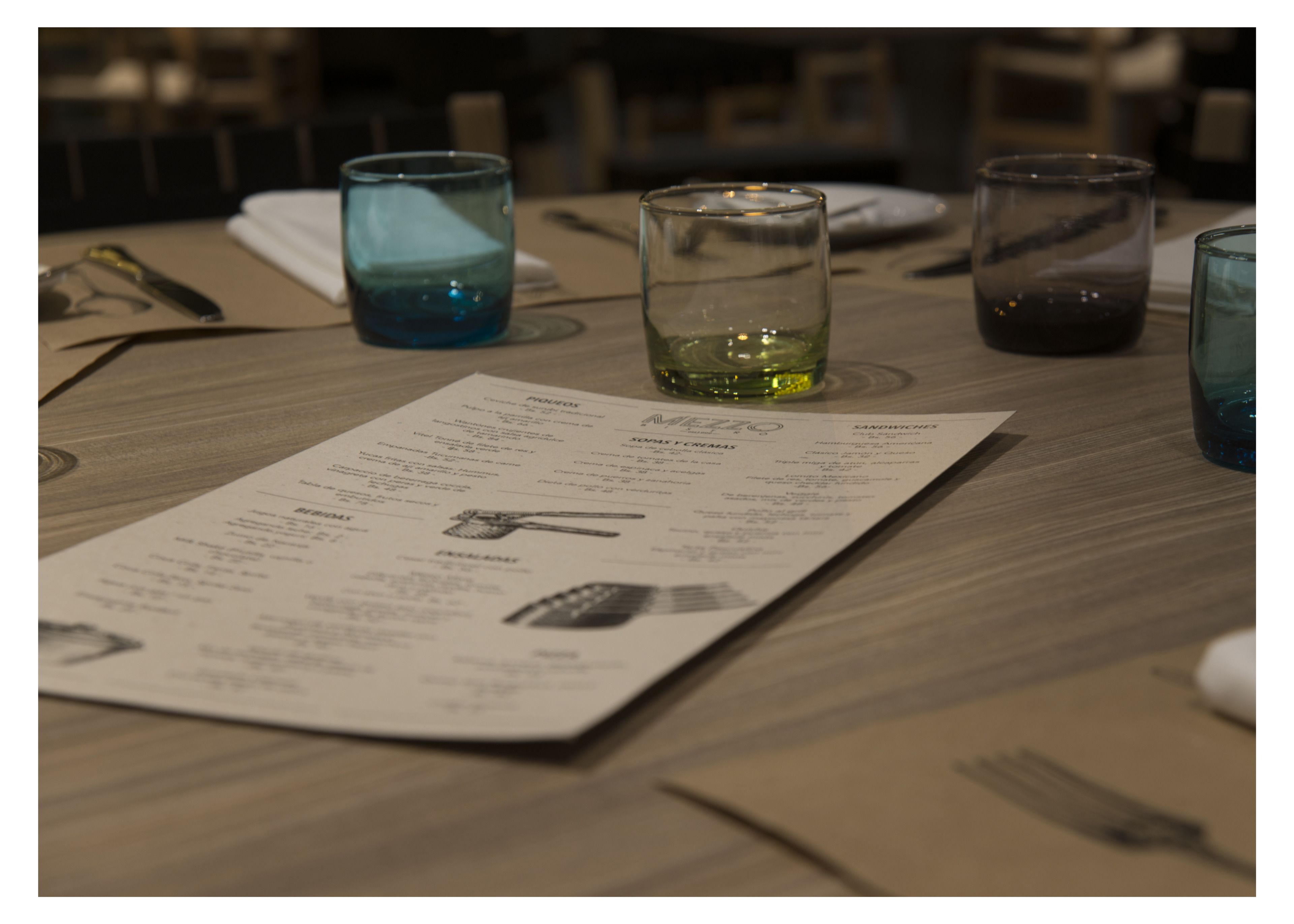 A menu on a wooden table with glasses and cutlery.