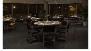 A restaurant with round tables and chairs, large windows, and potted plants. - Casa Grande Suites (La Paz)