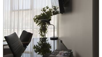 A modern office desk with a computer monitor, a lamp, a plant, and a stack of books.