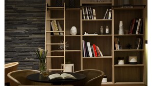 A modern living room with a stone accent wall, a wooden bookshelf, and a dining area with two chairs and a table. - Casa Grande Suites (La Paz)