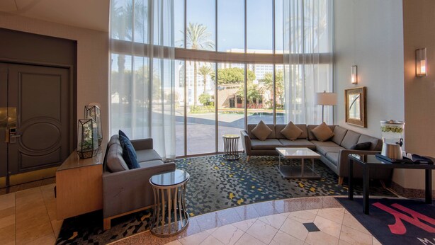 A spacious hotel lobby with a large seating area, a coffee table, and a view of the outdoor pool area. - Anaheim Marriott Suites (Garden Grove)