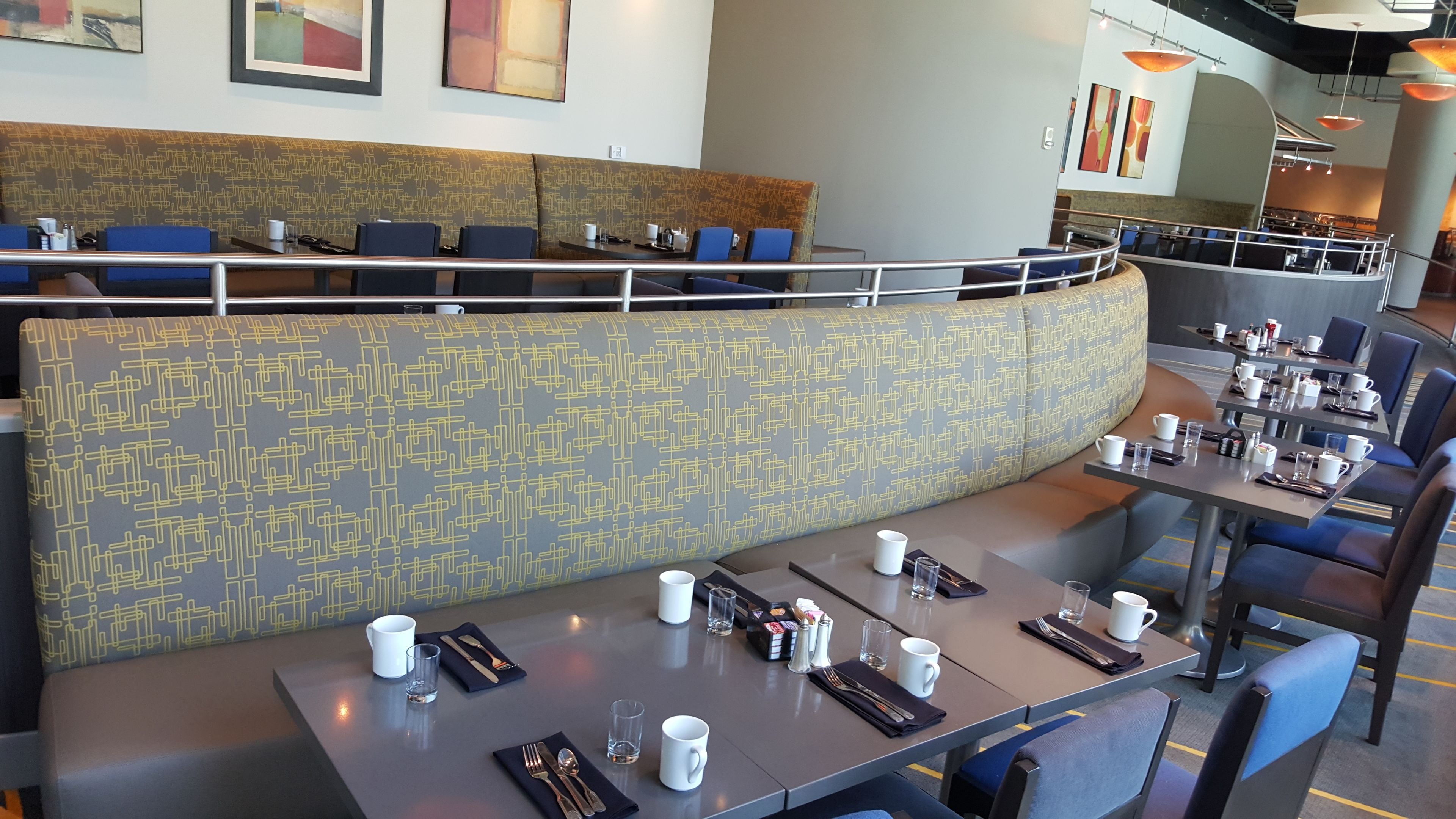 A modern restaurant with a patterned bench seating area, tables with dining essentials, and a view of the dining area.