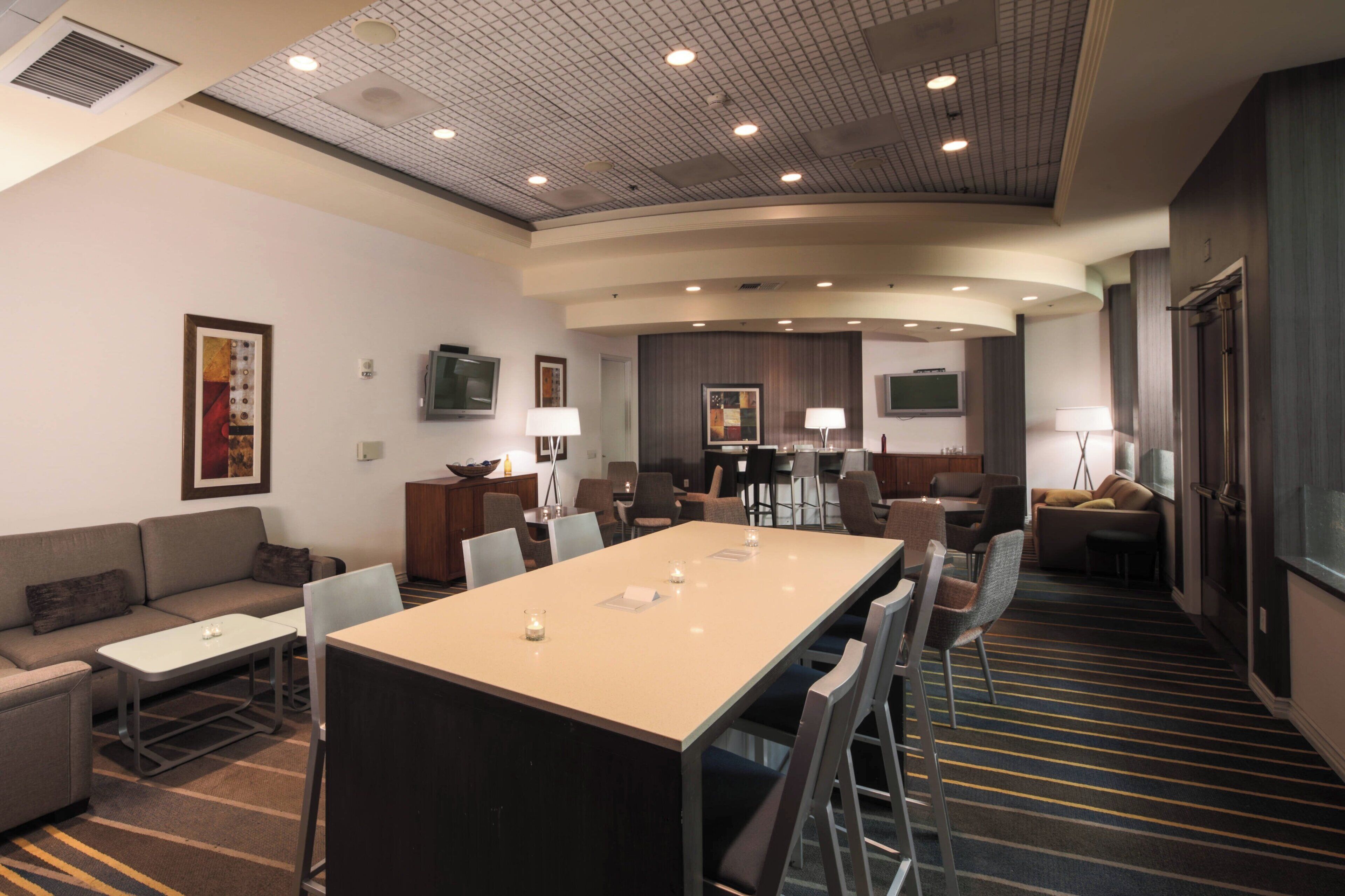 A modern hotel conference room with a long table, several chairs, a sofa, and a television.