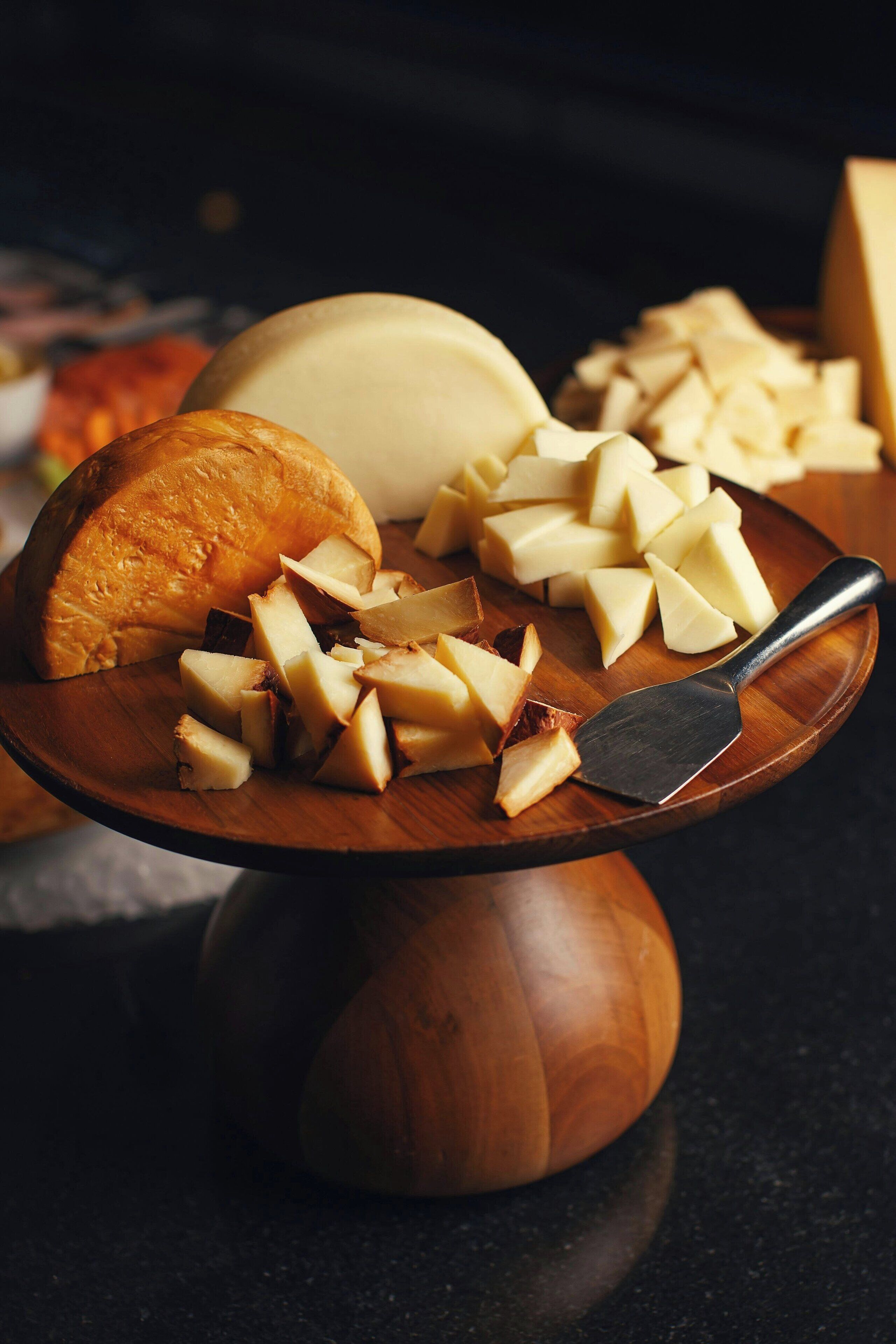 A wooden serving board with cheese and a cheese knife.
