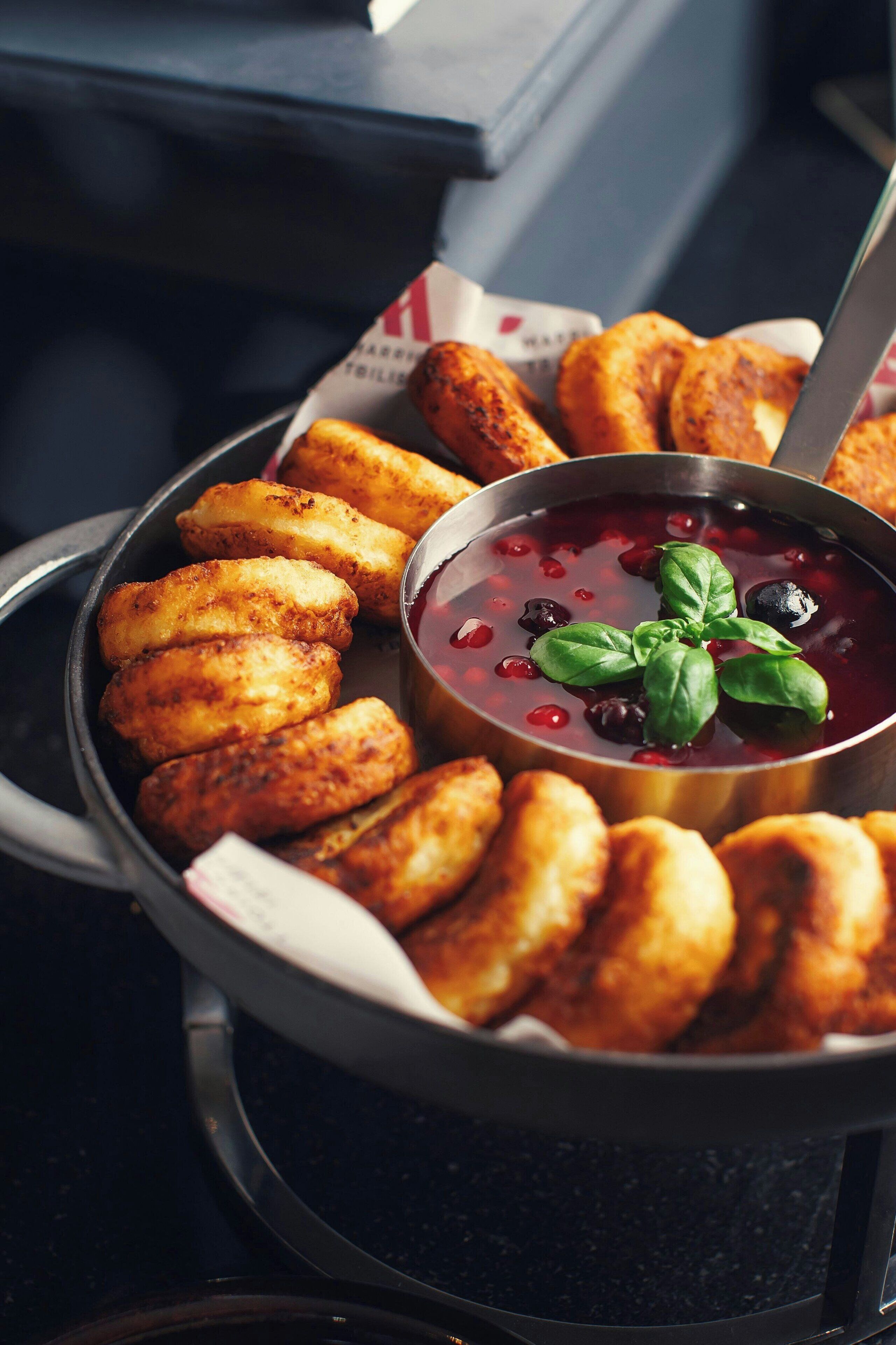 Una bandeja de alimentos fritos dorados y un tazón de salsa roja con hojas de albahaca.