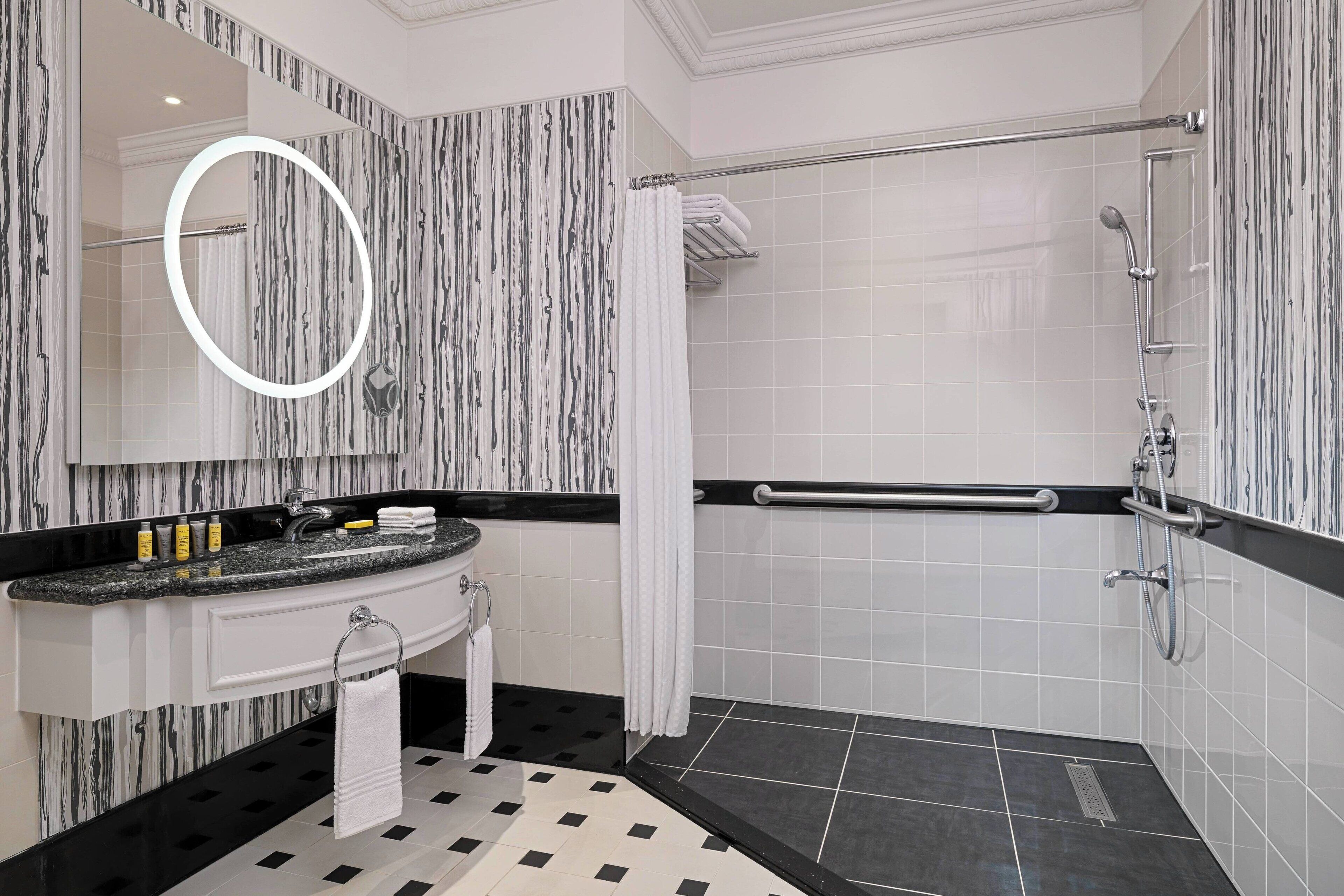 Une salle de bain moderne avec un meuble-lavabo, une douche équipée d’une barre d’appui et un sol carrelé.