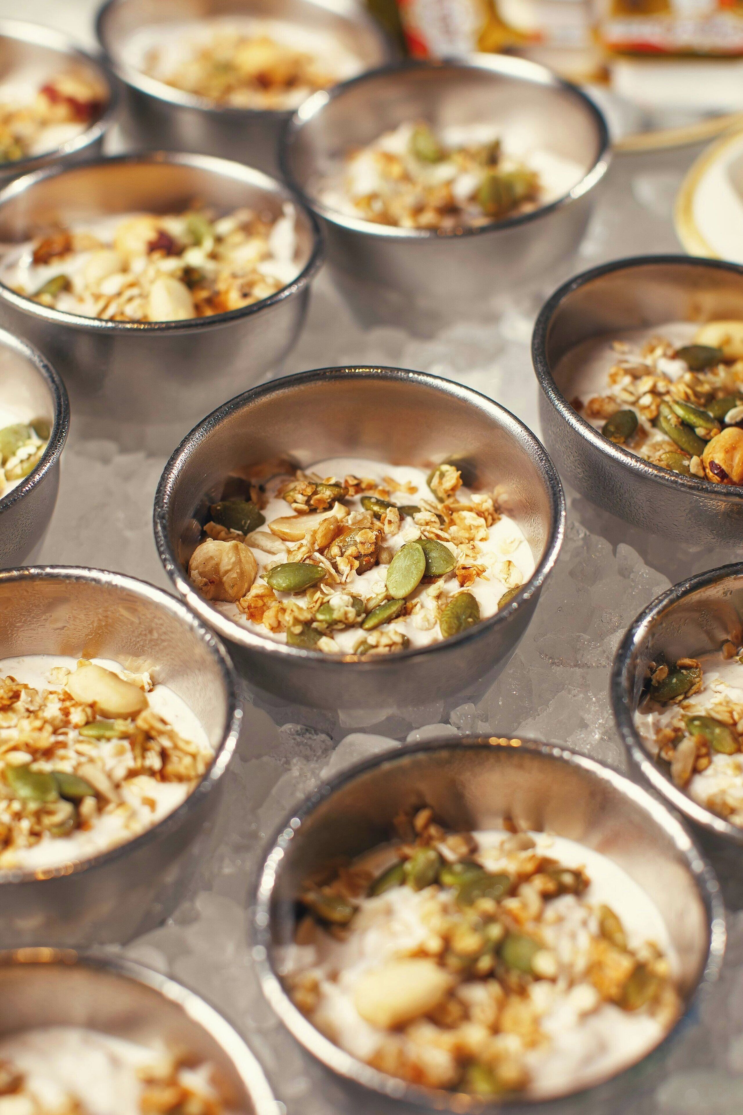 Varios recipientes pequeños con un plato a base de yogur, granola y semillas, dispuestos en una bandeja.