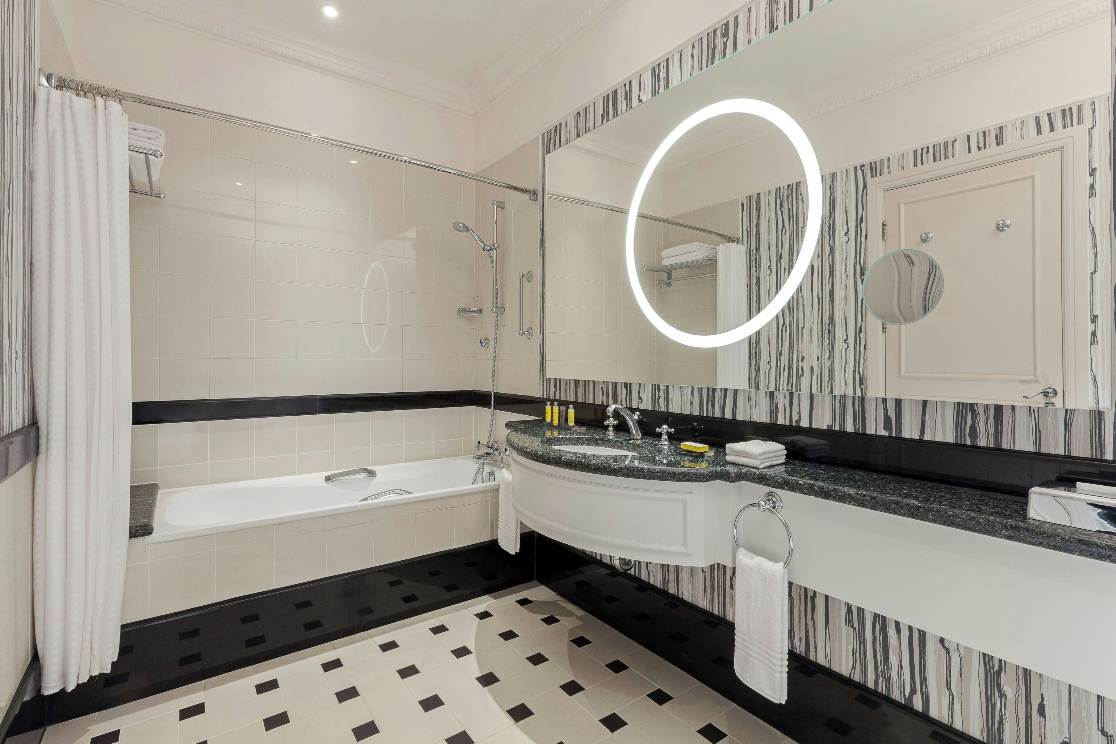 Ein modernes Badezimmer mit einer Badewanne, einem großen Spiegel mit runder Beleuchtung und einem gemusterten Boden.