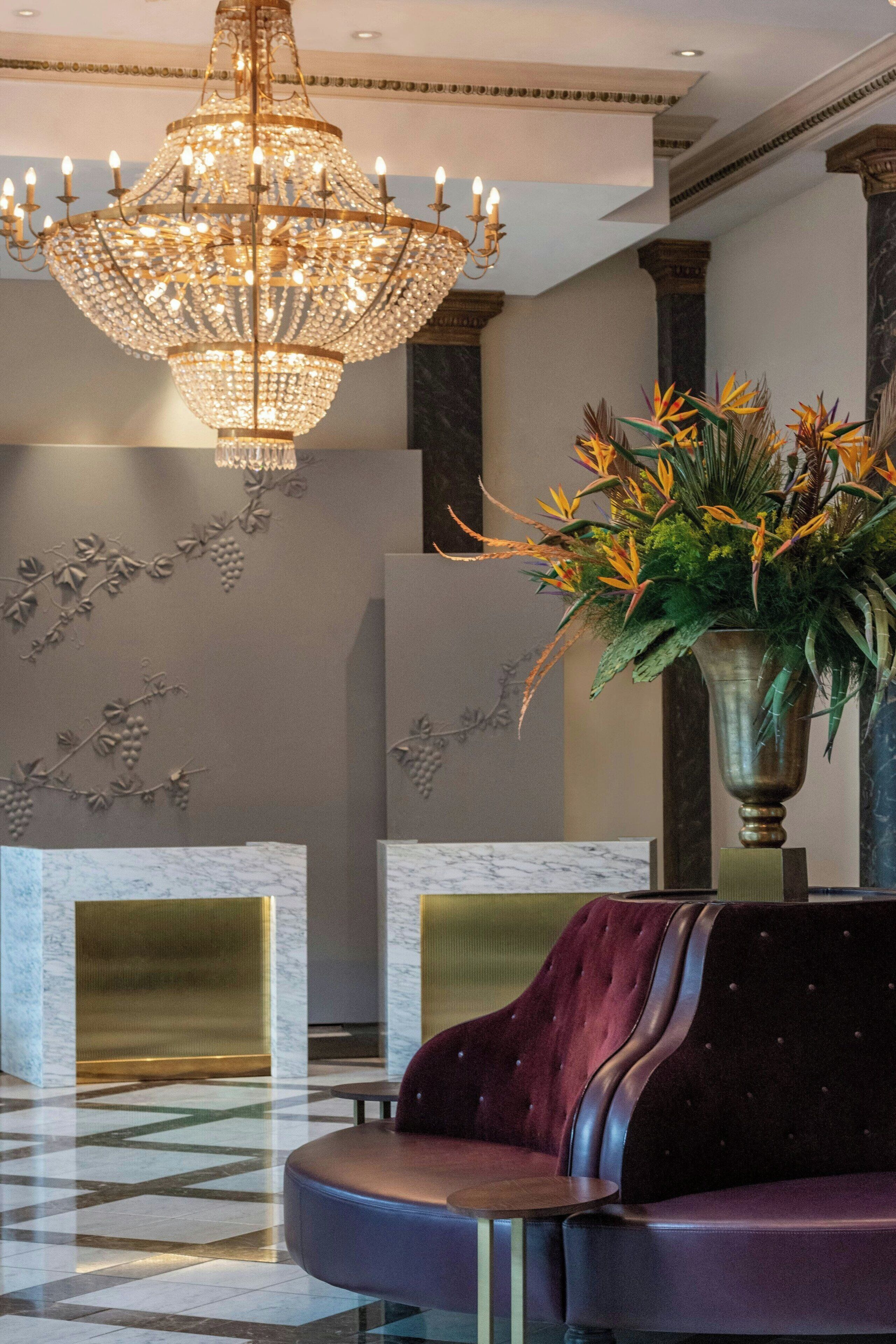 A lobby with a chandelier, a reception desk, a sofa, and a decorative wall with grapevine designs.