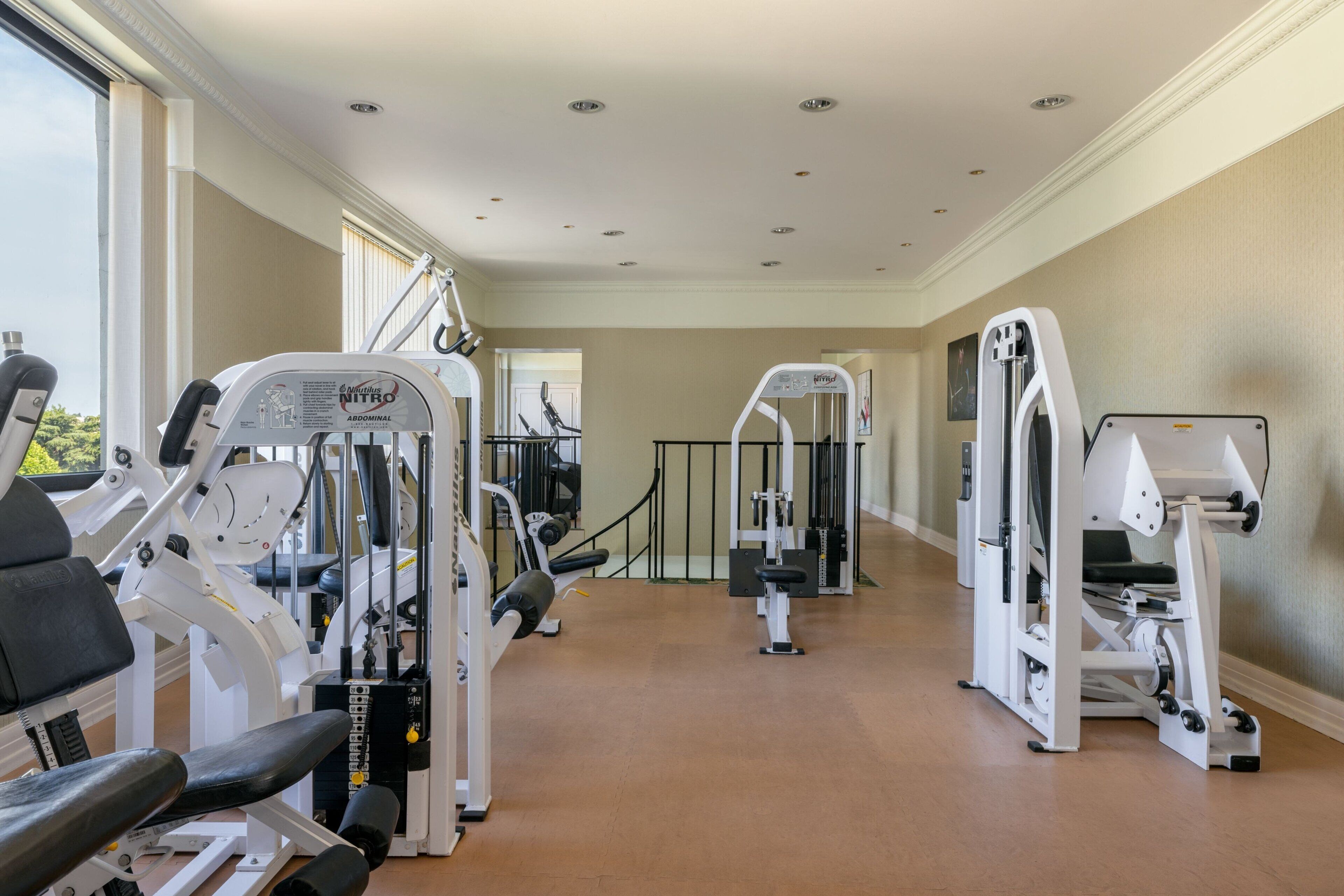 Une salle de sport équipée de divers appareils d’exercice, d’un miroir et offrant une vue sur l’extérieur grâce à de grandes fenêtres.